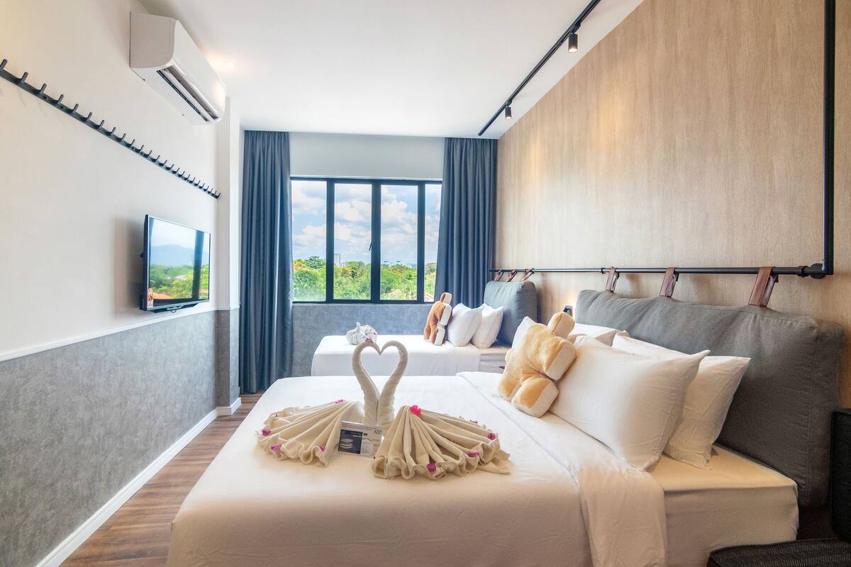 A hotel room with a bed, a TV, a large window, and a view of greenery.