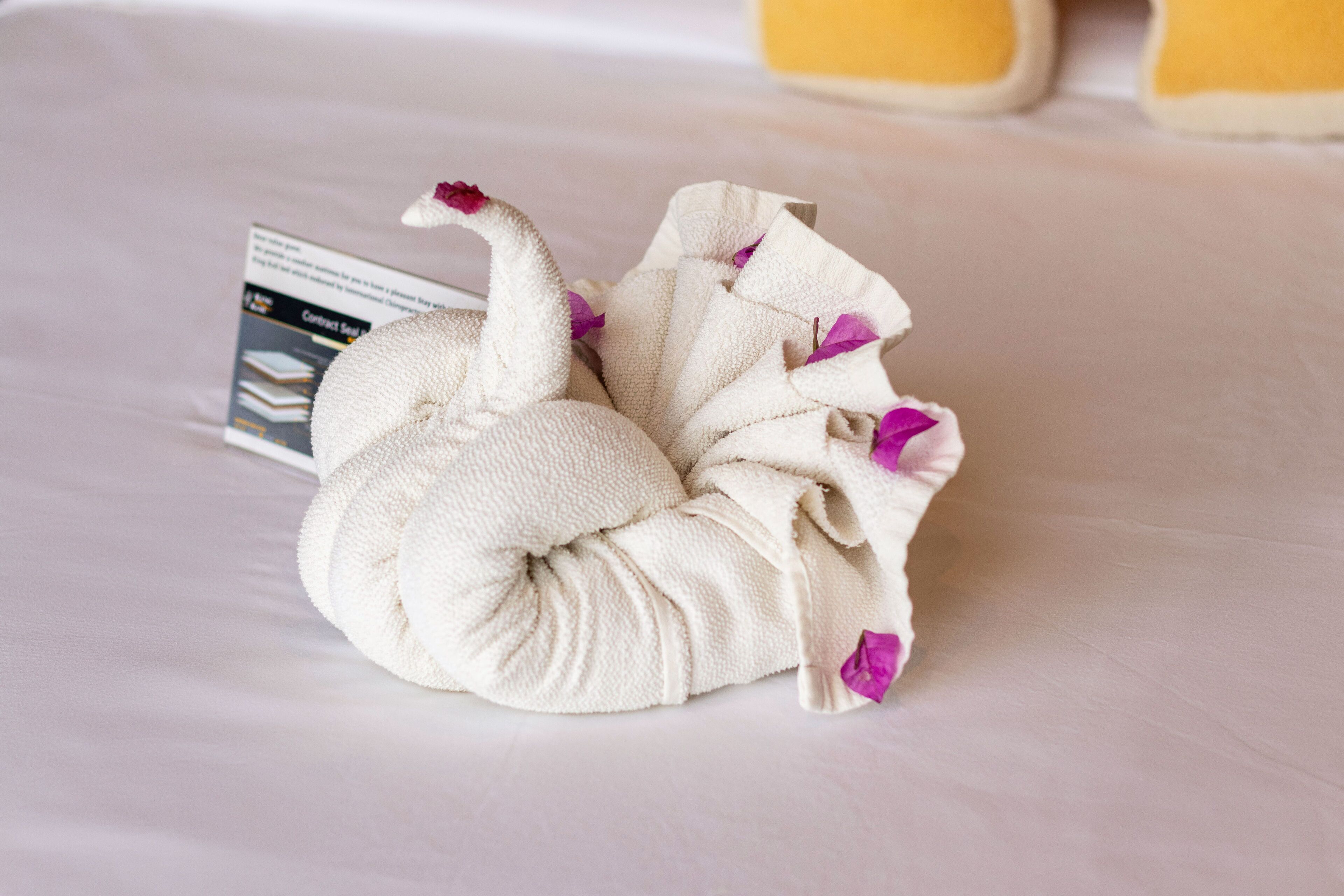 Una toalla con forma de cisne y flores púrpuras sobre una cama.