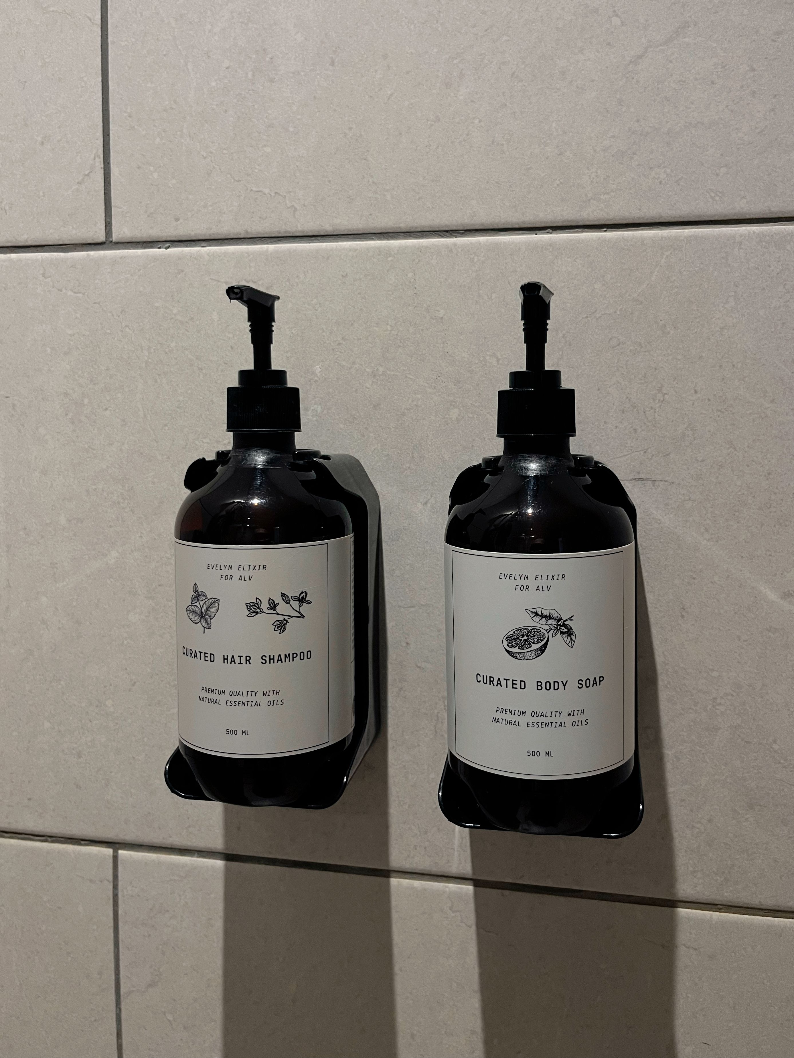Two bottles of Evelyn Elixir products, one labeled Curated Hair Shampoo and the other Curated Body Soap, both with a 500 ml volume.