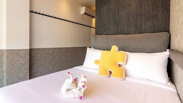 A hotel room with a neatly made bed, a large pillow, a decorative swan, and a wall-mounted air conditioning unit.