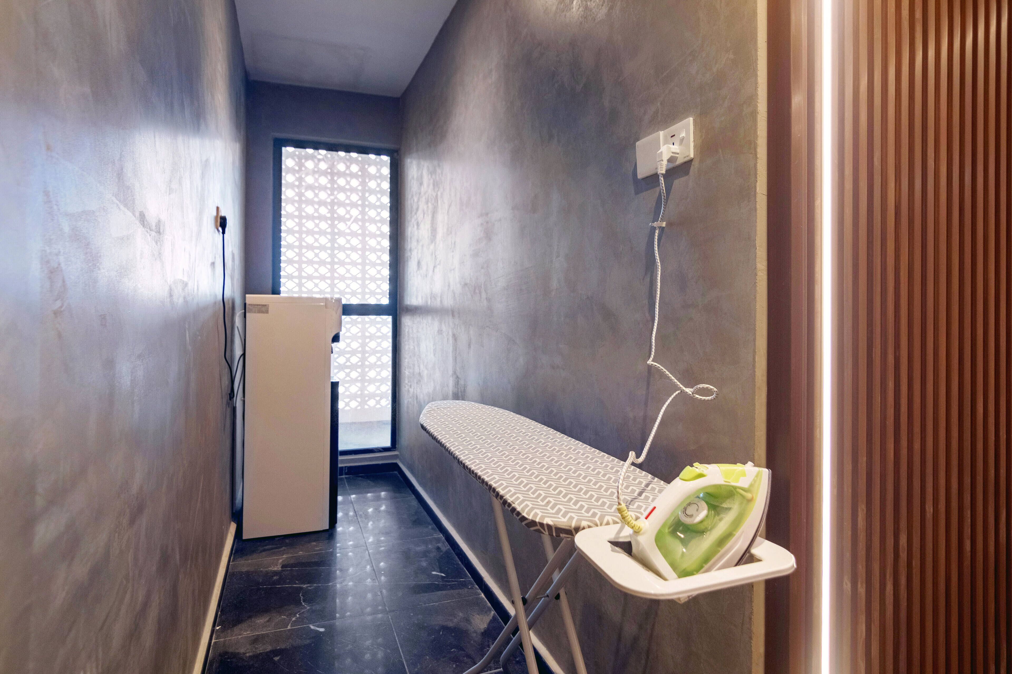 A narrow hallway with a large window, a wall-mounted ironing board, and a refrigerator.
