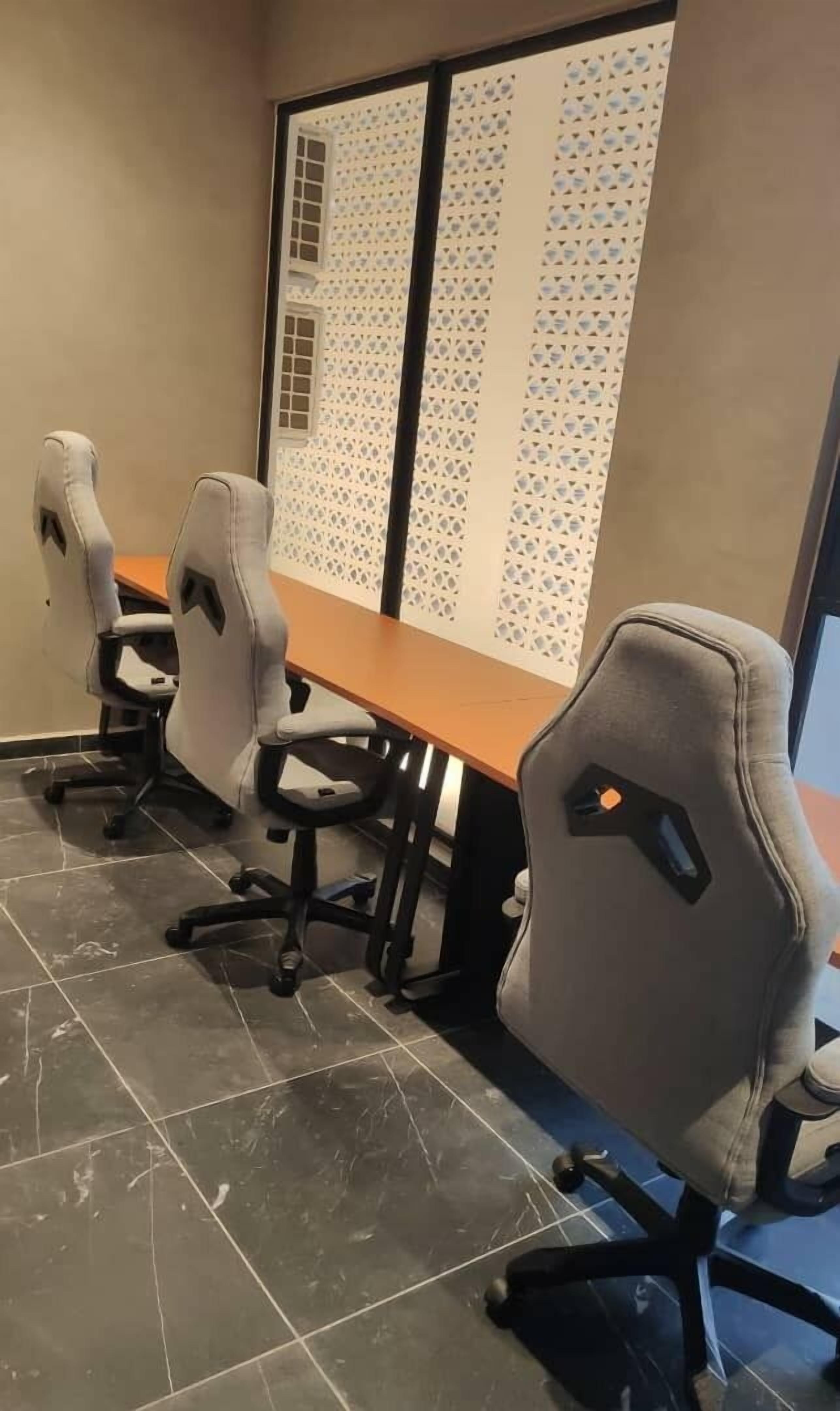Een vergaderruimte met een lange tafel en vier grijze bureaustoelen.