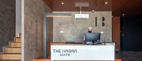 A reception desk labeled "The Ibagan Suite" with a modern design, wooden flooring, and a staircase to the left.
