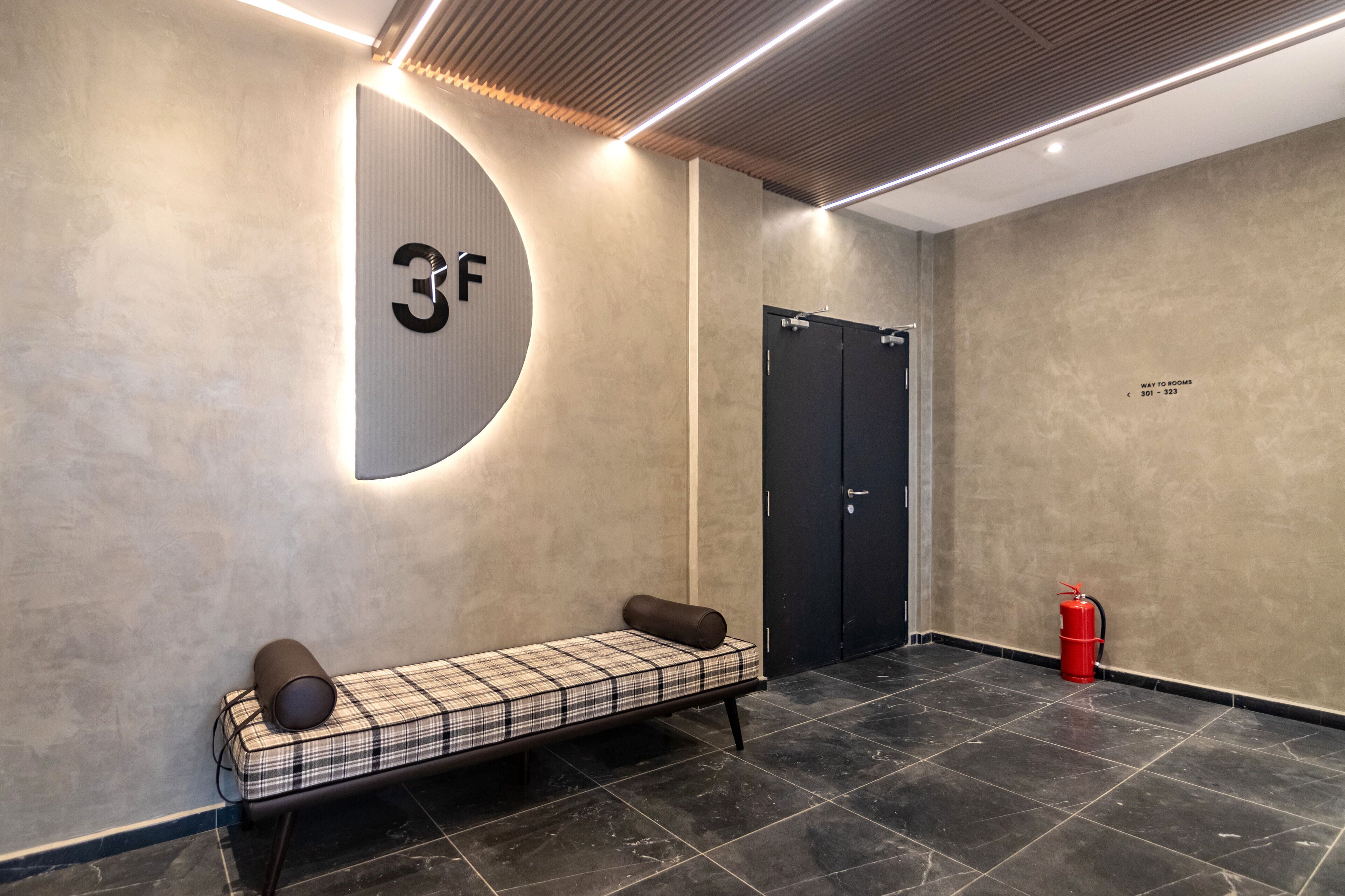 Un hall d’entrée moderne avec un banc, une enseigne fixée au mur, une porte et un extincteur.