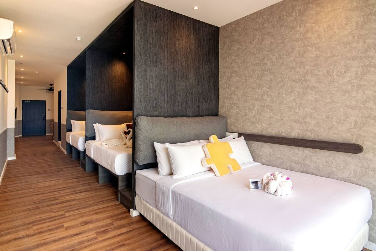 A hotel room with a large bed, a smaller bed, and a sofa bed. There is a wooden floor and a textured wall.