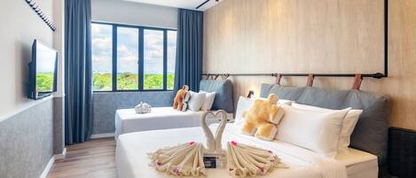 A hotel room with two beds, a large window, a flat-screen TV, and a view of greenery outside.