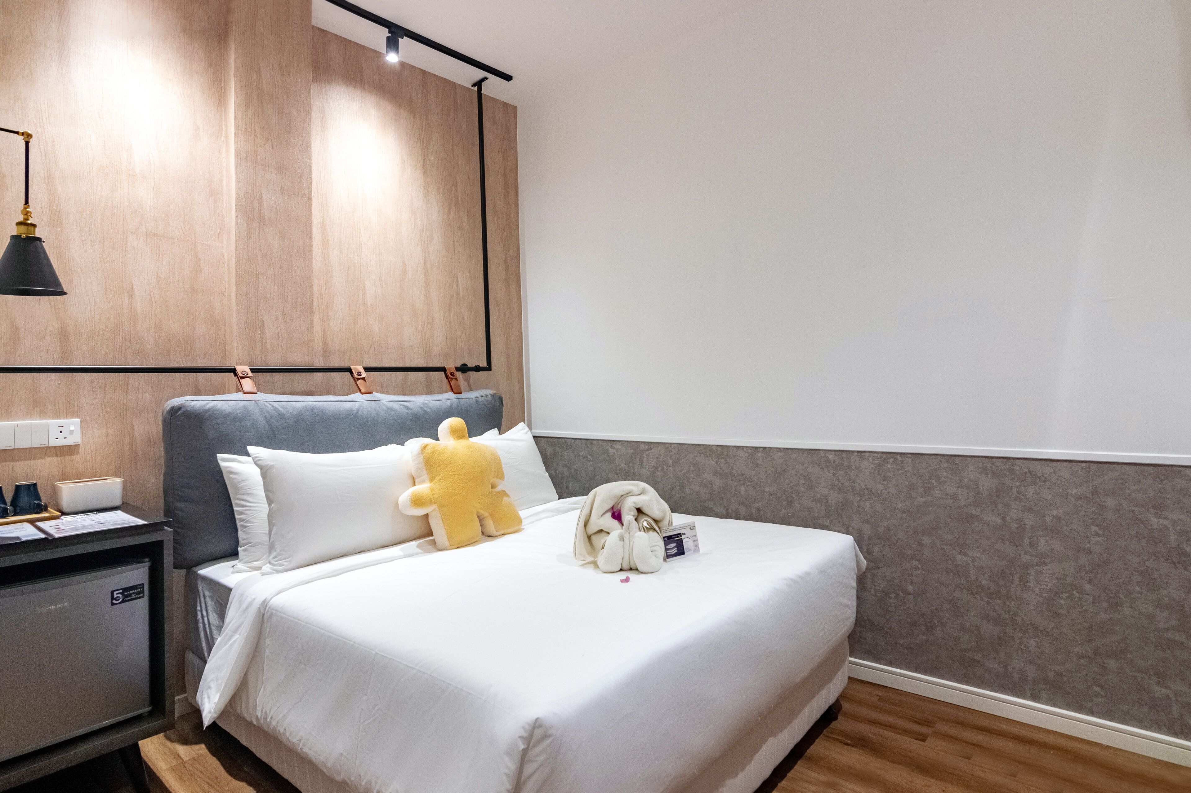 Una habitación de hotel con cama, mesita de noche, lámpara y un peluche.