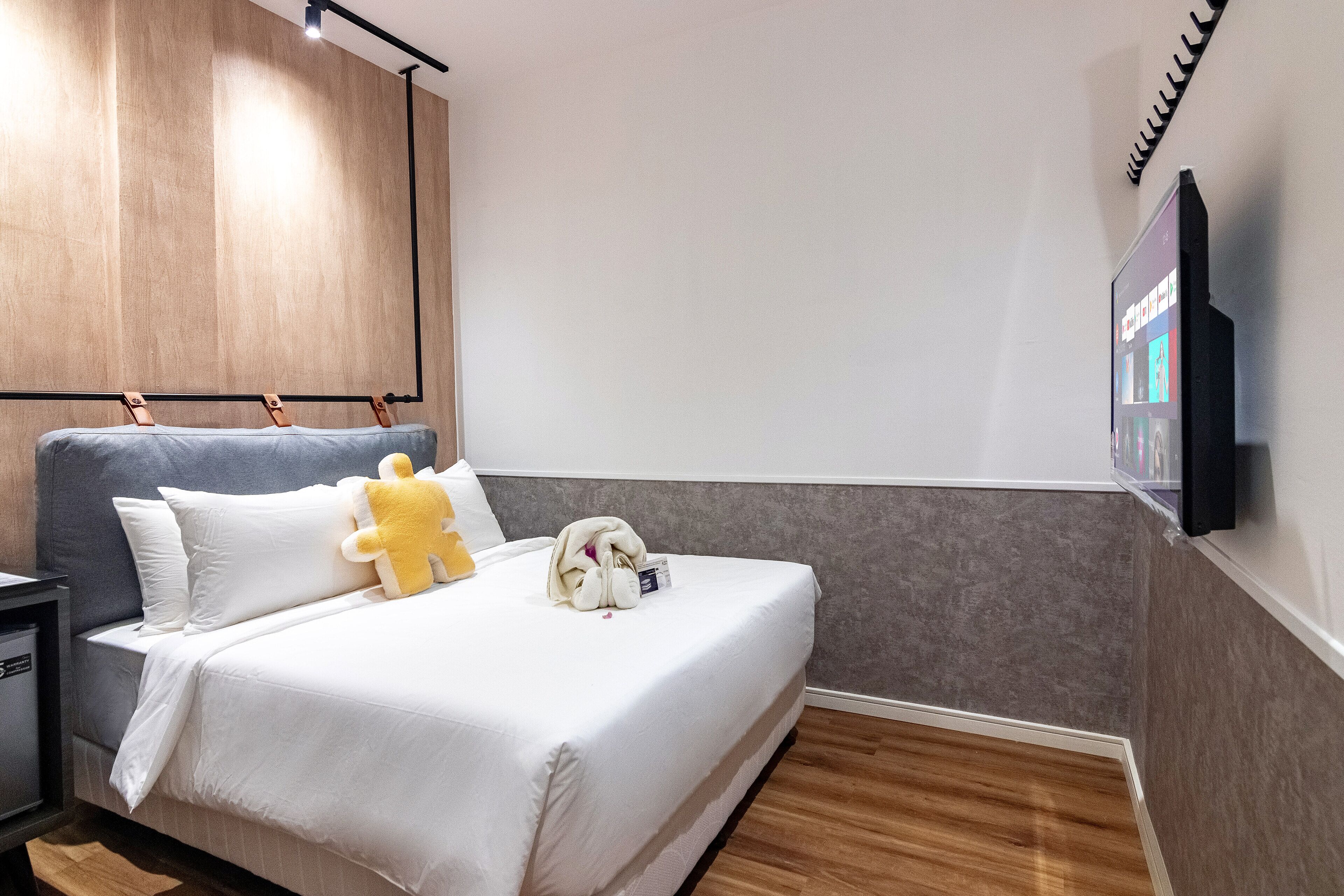 A modern hotel room with a large bed, a flat-screen TV mounted on the wall, and a wooden headboard.