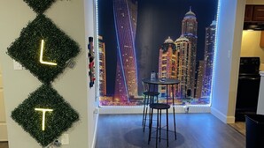 Ein modernes Interieur mit einem Stadtblick-Mural, einem Tisch mit Stühlen und einer Wand mit leuchtenden Buchstaben.