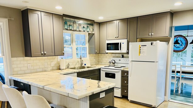 A modern kitchen with a central island, bar stools, a microwave, stove, and refrigerator.