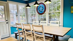 A dining area with a wooden table and chairs, large windows with a view of trees, and pendant lights.