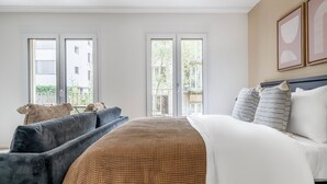 Une chambre d’hôtel moderne, dotée d’un grand lit, d’un canapé et de deux fenêtres donnant sur l’extérieur.