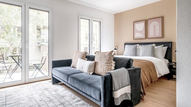 Une chambre à coucher moderne avec un lit, un canapé gris et une grande fenêtre.