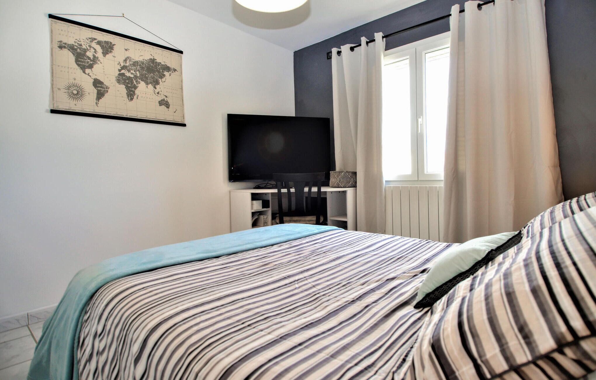 A bedroom with a bed, a TV, a desk, and a world map on the wall.