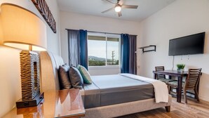 A hotel room with a bed, a desk, a chair, a TV, and a window with curtains. - Unit 25 Waena Inn - Maui Private Suite (Wailuku)