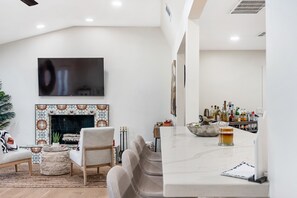 Una sala de estar moderna con chimenea, una zona de bar con botellas y un televisor de pantalla plana montado en la pared.