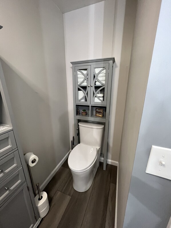 A compact bathroom with a toilet, a cabinet with glass doors, and a toilet brush.