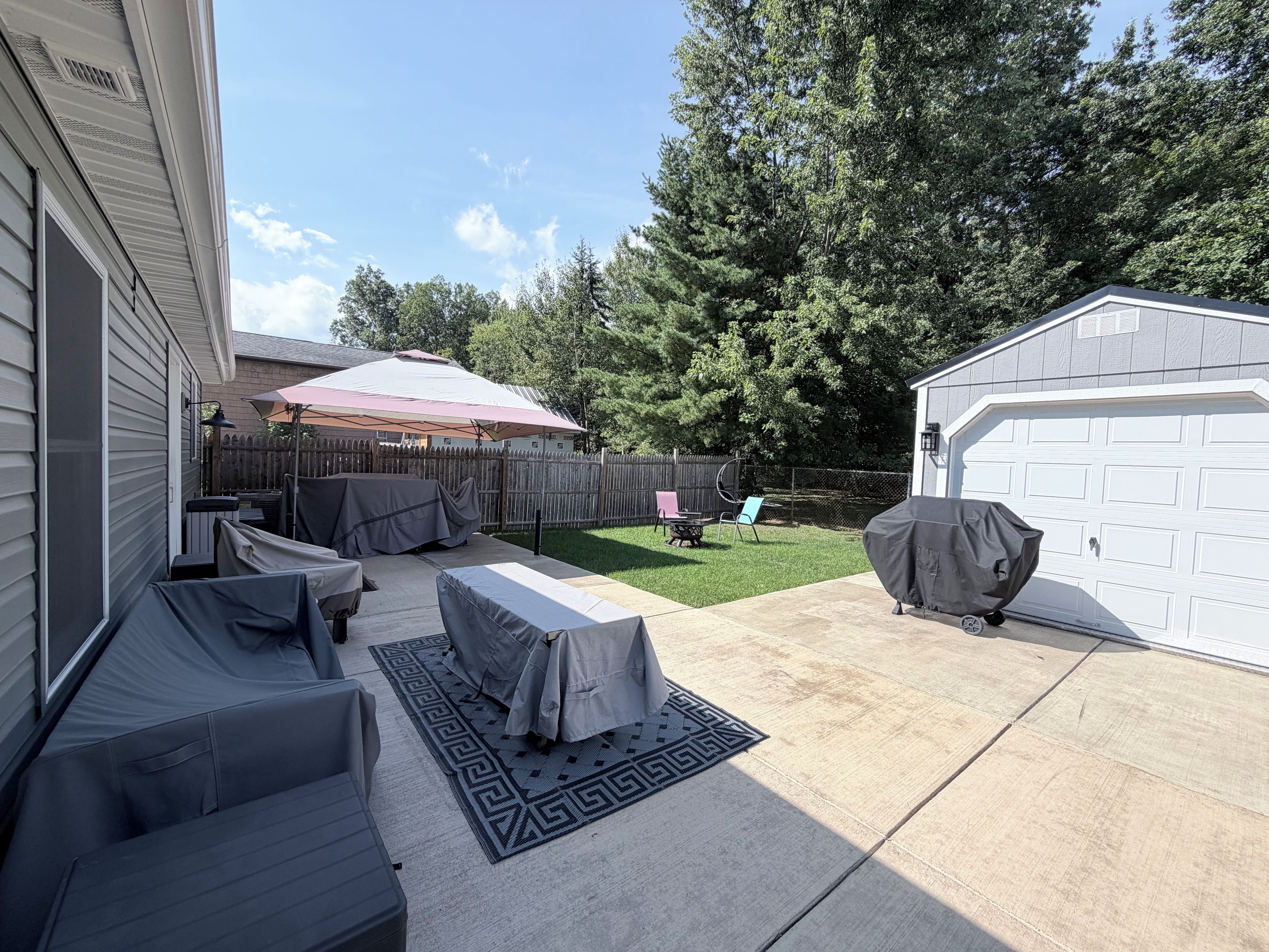 A backyard with a covered patio area, a barbecue grill, and a garage.