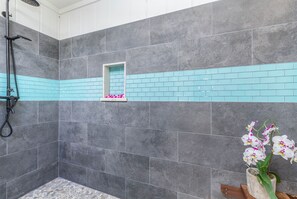 Un baño con baldosas grises, una ventana pequeña y una orquídea en maceta.