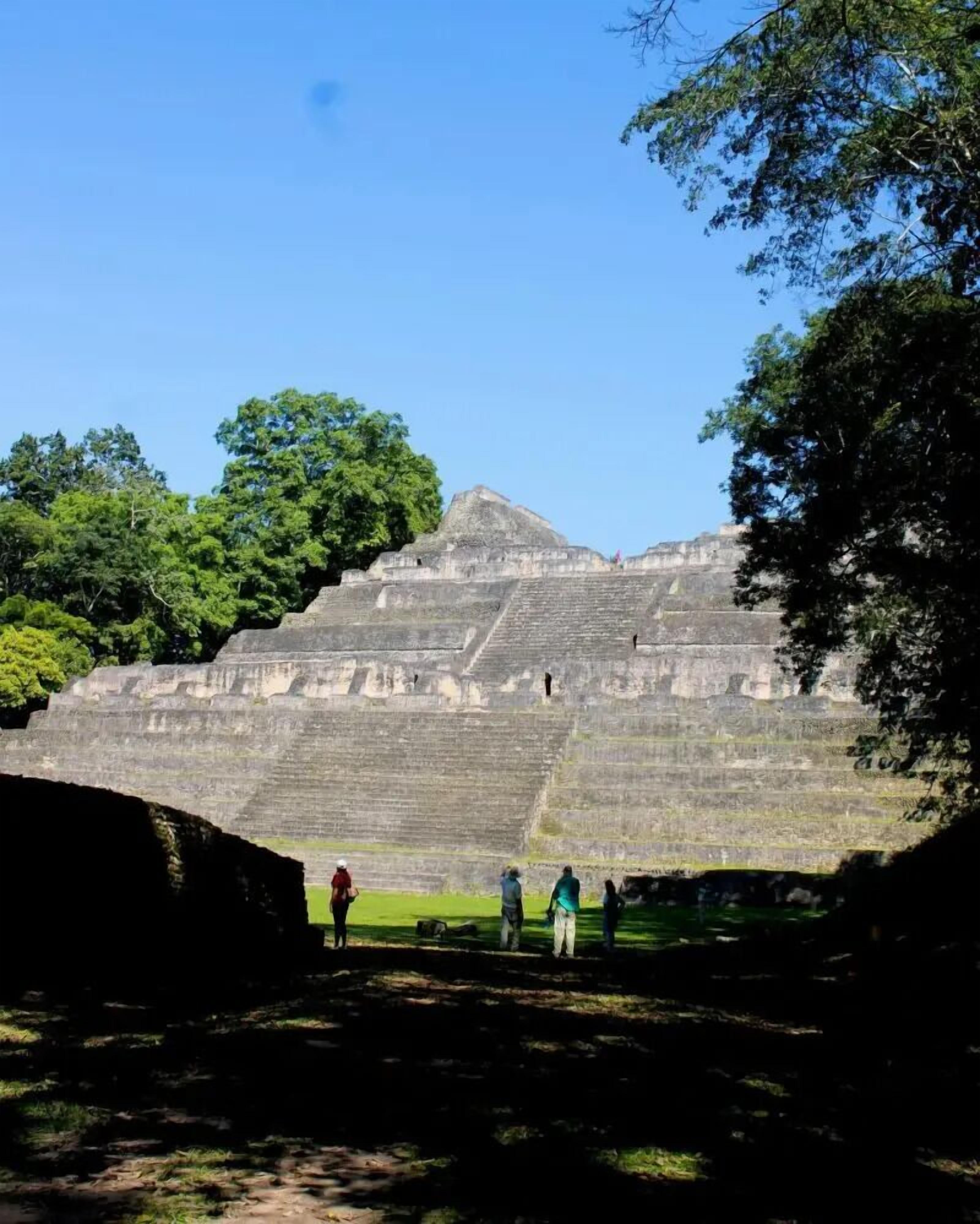 A large stone pyramid structure with multiple levels, surrounded by lush green trees.