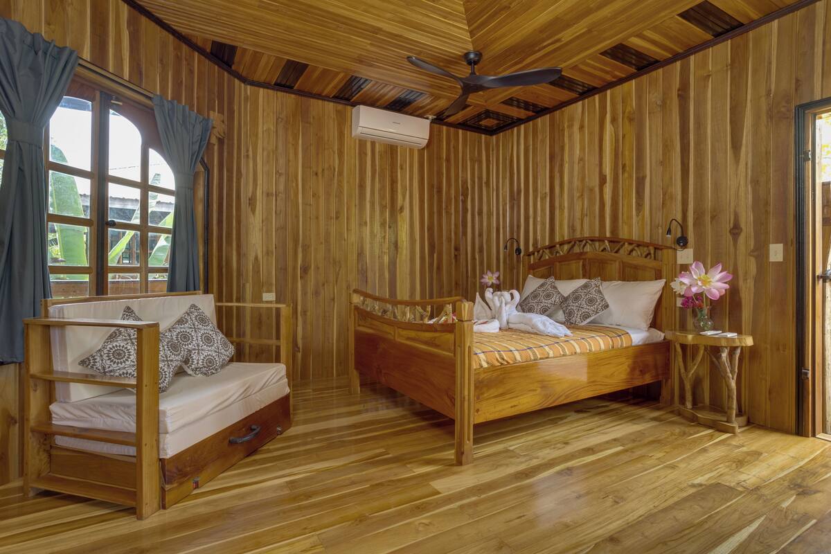 A wooden room with a bed, a chair, and a small table.