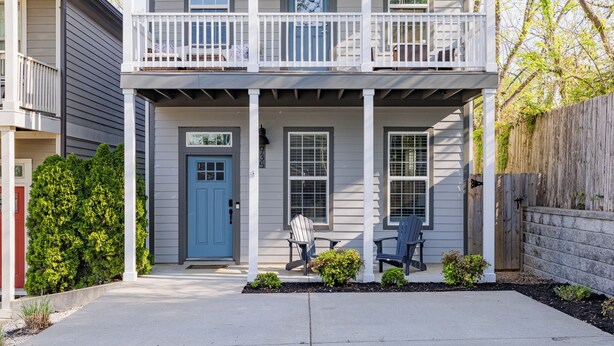 A two-story house with a porch, a blue door, and two chairs outside.