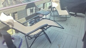 En balkong med ett bord och två stolar, en grill och utsikt över de omkringliggande byggnaderna.