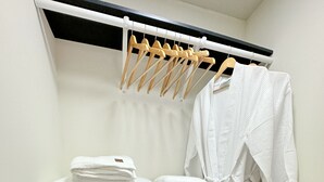 A small laundry area with a drying rack, a shelf with folded towels, and a hanging rack with clothes.