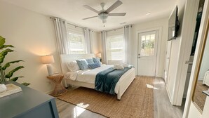 A modern bedroom with a bed, a ceiling fan, and a large window with blinds.
