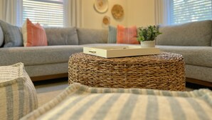 A living room with a grey sofa, a woven ottoman, and a small potted plant.