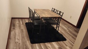 Ein Essbereich mit Holztisch und -stühlen, einem schwarzen Teppich und Holzboden.