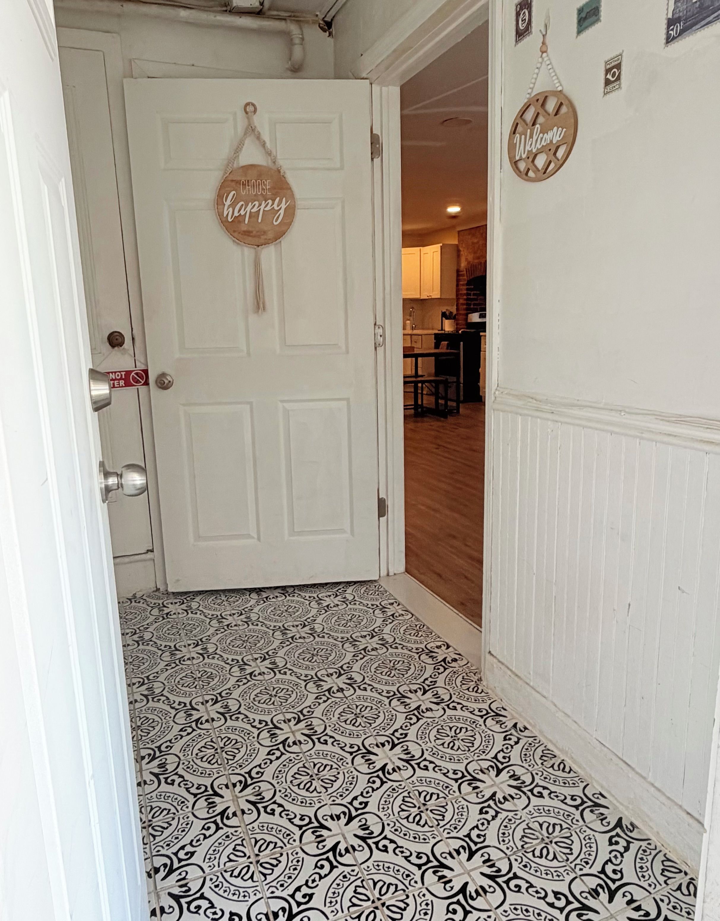 Un pasillo con piso estampado, una puerta blanca con un letrero que dice 'Choose Happy' y un cartel de 'Welcome' en la pared.