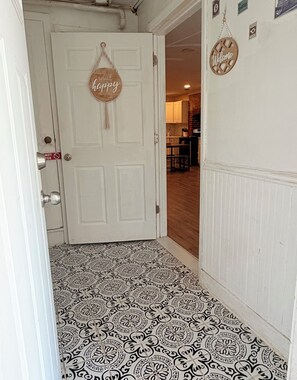 A hallway with patterned flooring, a white door with a 'Choose Happy' sign, and a 'Welcome' sign on the wall.