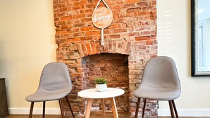 A room with a brick fireplace, two grey chairs, a small table with a plant, and a 'Choose happy' sign. - Charming Brick Row House close to NYC (Bayonne)