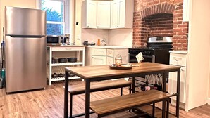 A modern kitchen with a brick wall, white cabinets, and a stainless steel refrigerator. - Charming Brick Row House close to NYC (Bayonne)