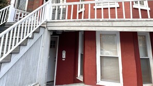 A red brick building with white trim, a balcony, and a staircase leading to the entrance. - Charming Brick Row House close to NYC (Bayonne)