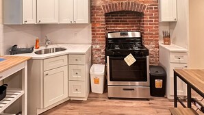 A compact kitchen with white cabinets, a brick backsplash, a stainless steel stove, and a wooden countertop. - Charming Brick Row House close to NYC (Bayonne)