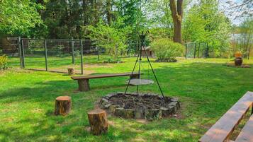 A fenced outdoor area with a fire pit, benches, and a swing set.