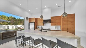 A modern kitchen with a large island, bar stools, and a view of a garden. - Ultra modern contemporary Luxe (Palm Springs)