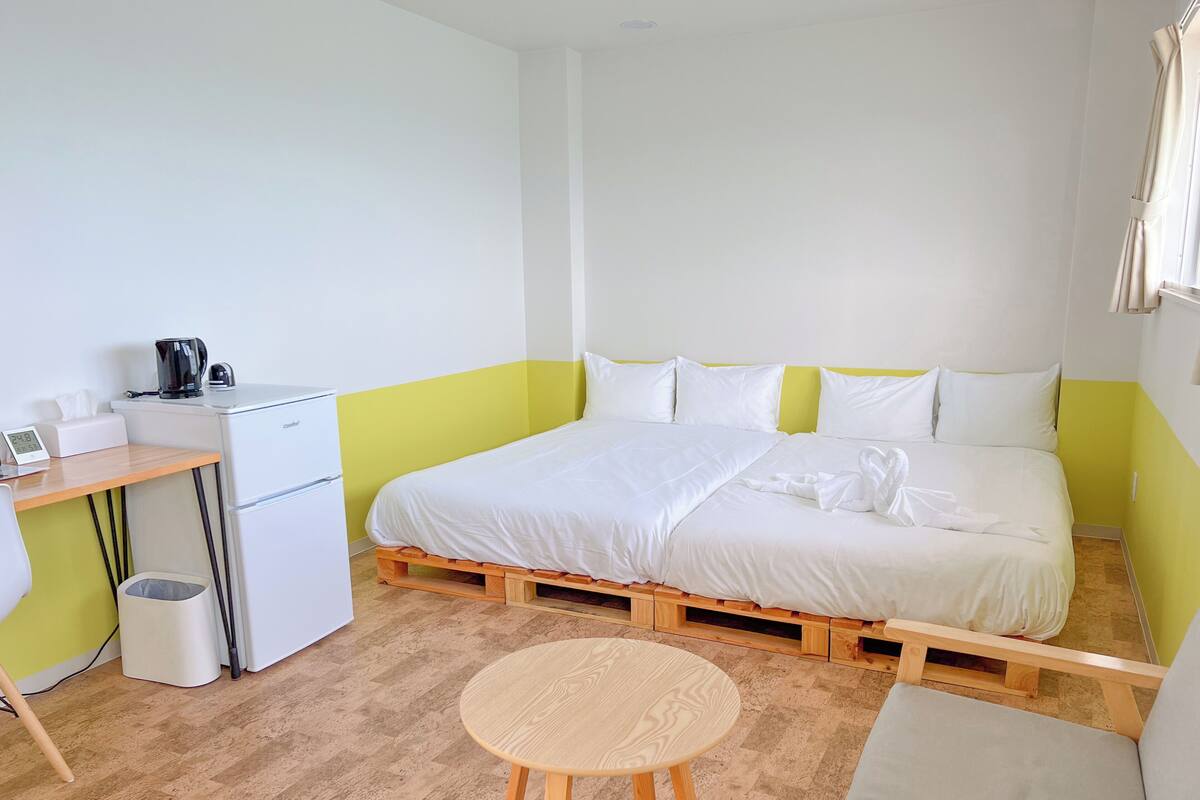 Ein Schlafzimmer mit einem Bett, einem kleinen Schreibtisch, einem Stuhl, einem runden Holztisch und einem Mülleimer.