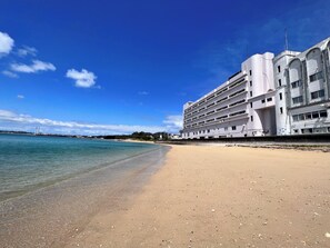 A beachfront hotel with multiple floors, a sandy beach in the foreground, and a clear blue sky. - My Beach Resort (Kin)
