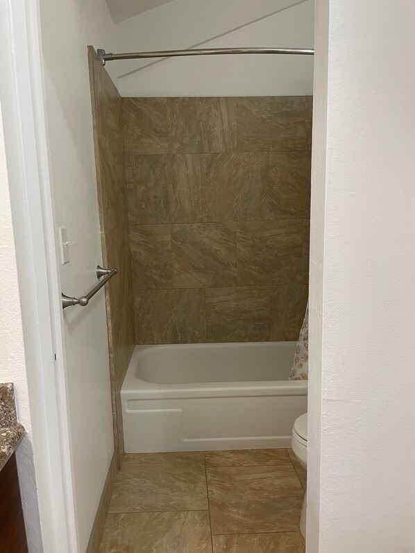 A bathroom with a bathtub, a shower curtain, and a toilet.