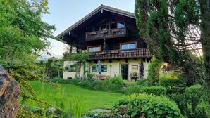 Ein traditionelles Holzhaus mit Balkon, umgeben von üppigem Grün und einem kleinen Teich.