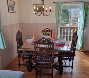 A dining area with a wooden table set for four, surrounded by ornate chairs. A chandelier hangs above, and a window with curtains is visible in the background. - Fewo Alpenglück und Heimatgfui (Schönau am Königssee)