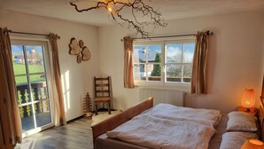 Ein Schlafzimmer mit einem großen Bett, zwei Fenstern, einem Sessel und einer Lampe.