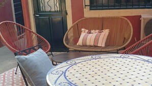 Eine Terrasse mit Korbmöbeln, einem runden Tisch mit gemustertem Unterblatt und einem roten Baldachin.