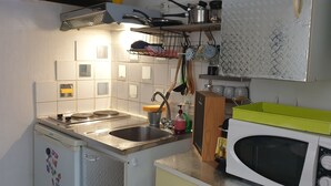 Eine kleine Küche mit Spüle, Herd und Mikrowelle. Über dem Herd hängen Kochutensilien und ein Regal mit Töpfen und Pfannen.