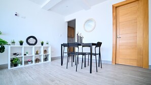 Un interior moderno con zona de comedor, puerta de madera y estantería blanca con plantas.