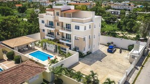 Un edificio residencial de varios pisos con piscina, mobiliario exterior y zona de estacionamiento vigilada.