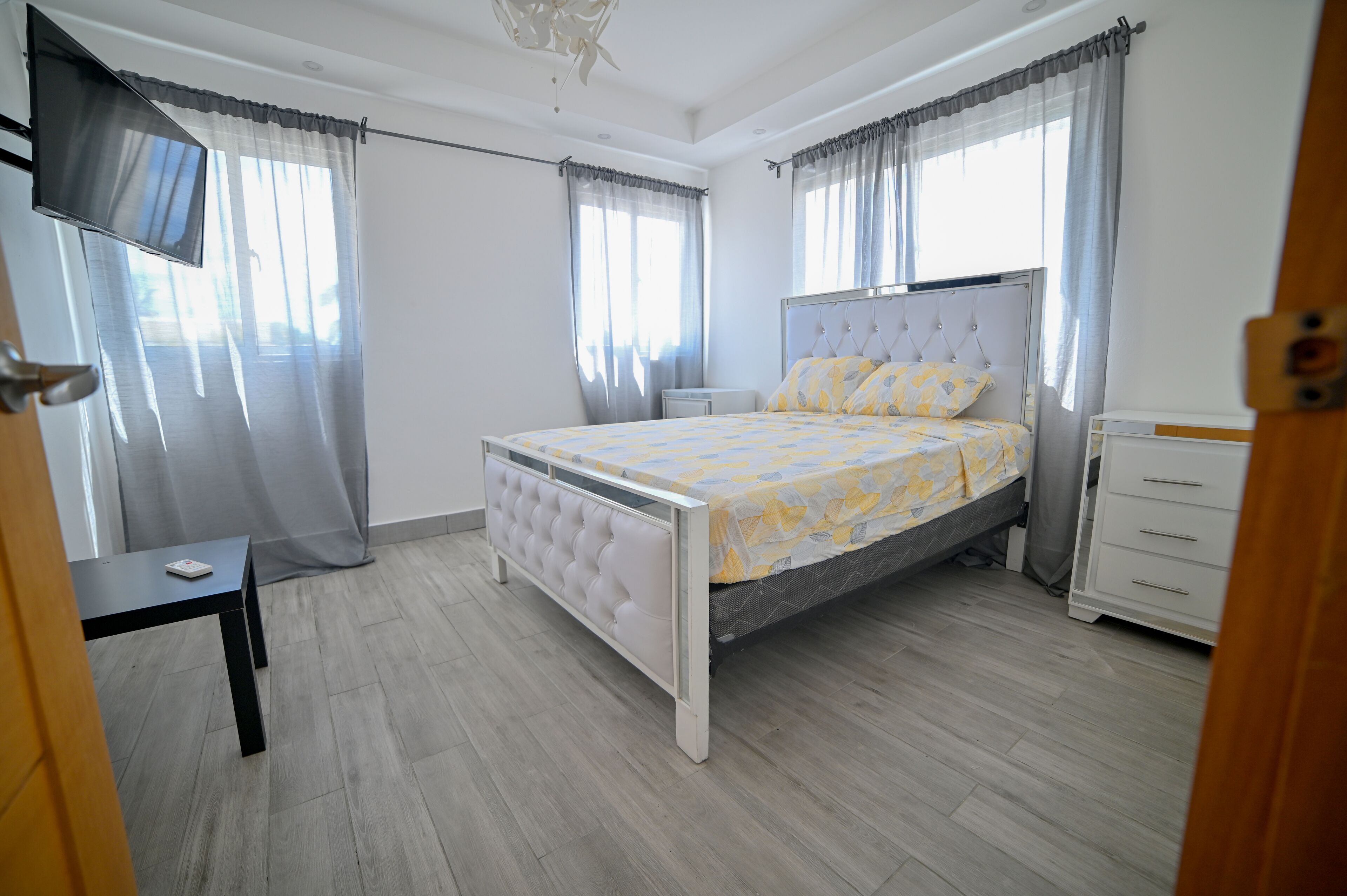 Ein Schlafzimmer mit Bett, Nachttisch, Fernseher und Vorhängen.
